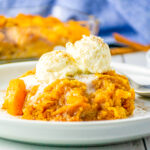 Peach cobbler topped with ice cream in a white dish.