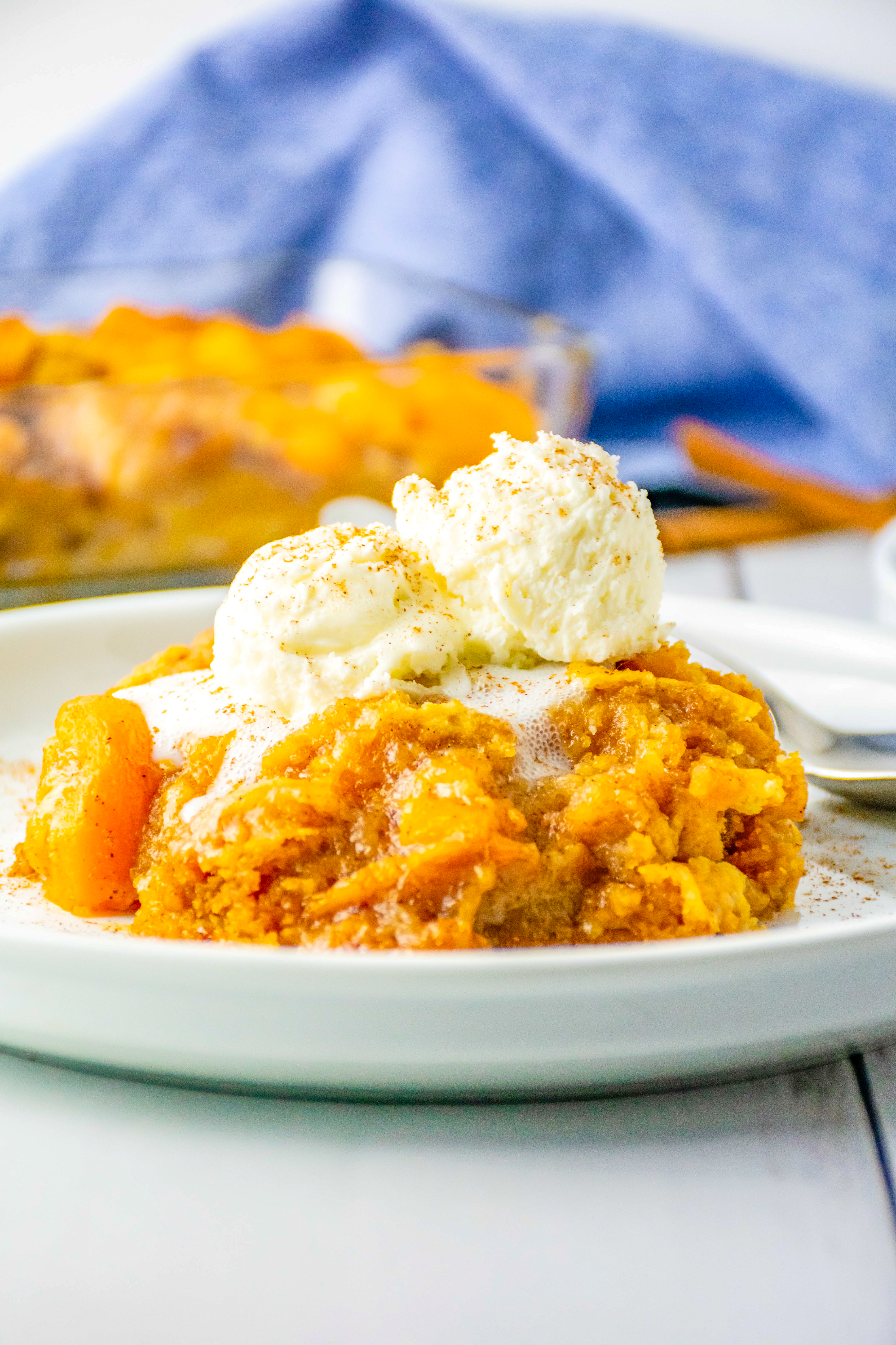 Peach cobbler topped with ice cream in a white dish.