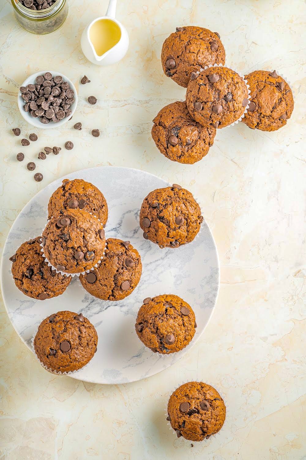 Chocolate muffins displayed on a white background next two a bowl of chocolate chips. 