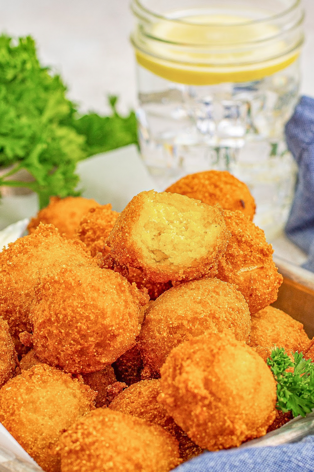 Hush puppies on a galvanized tray sitting a table next to a glass of water with lemon and a blue napkin.