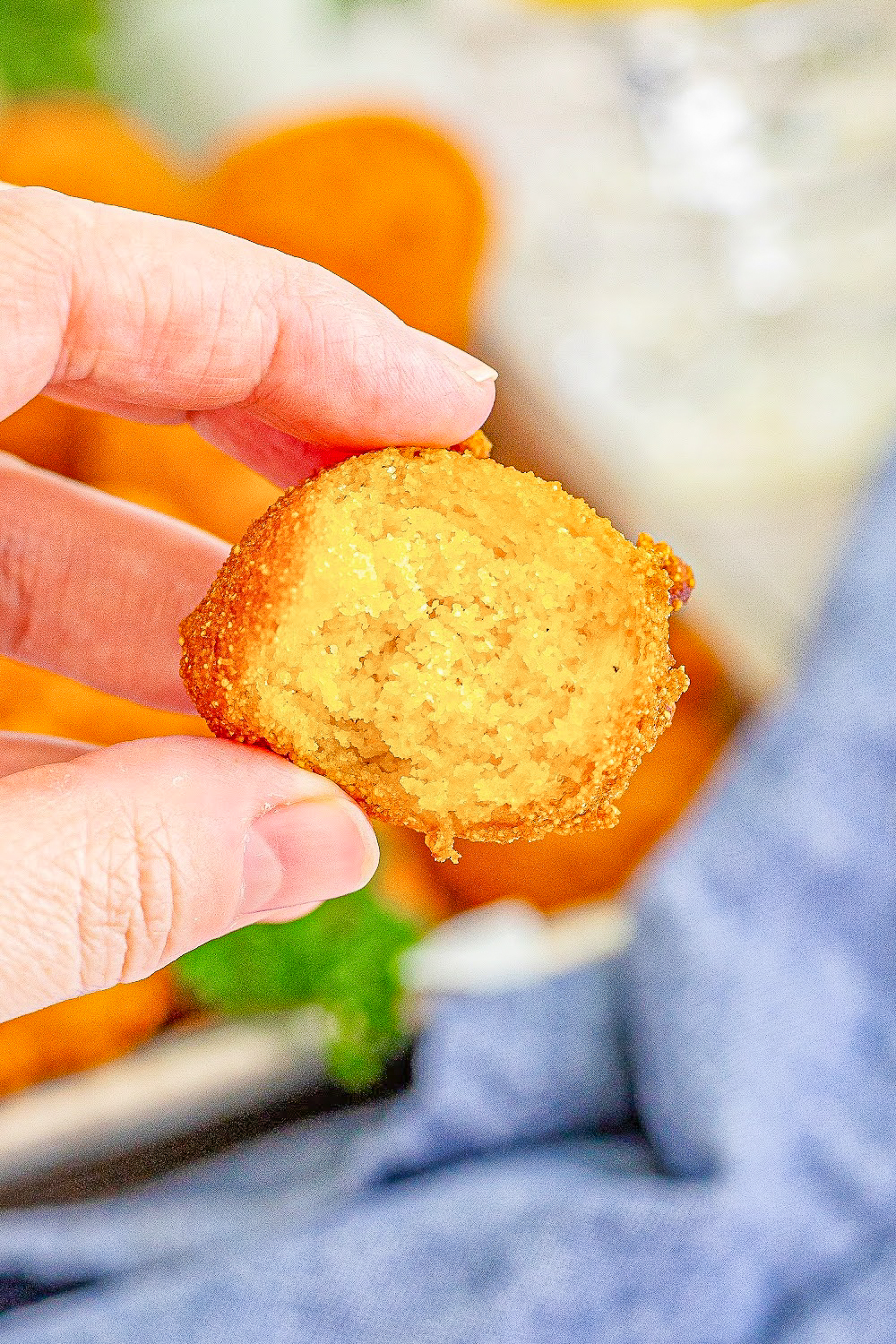A woman's hand hold a single hush puppy with a missing bite.