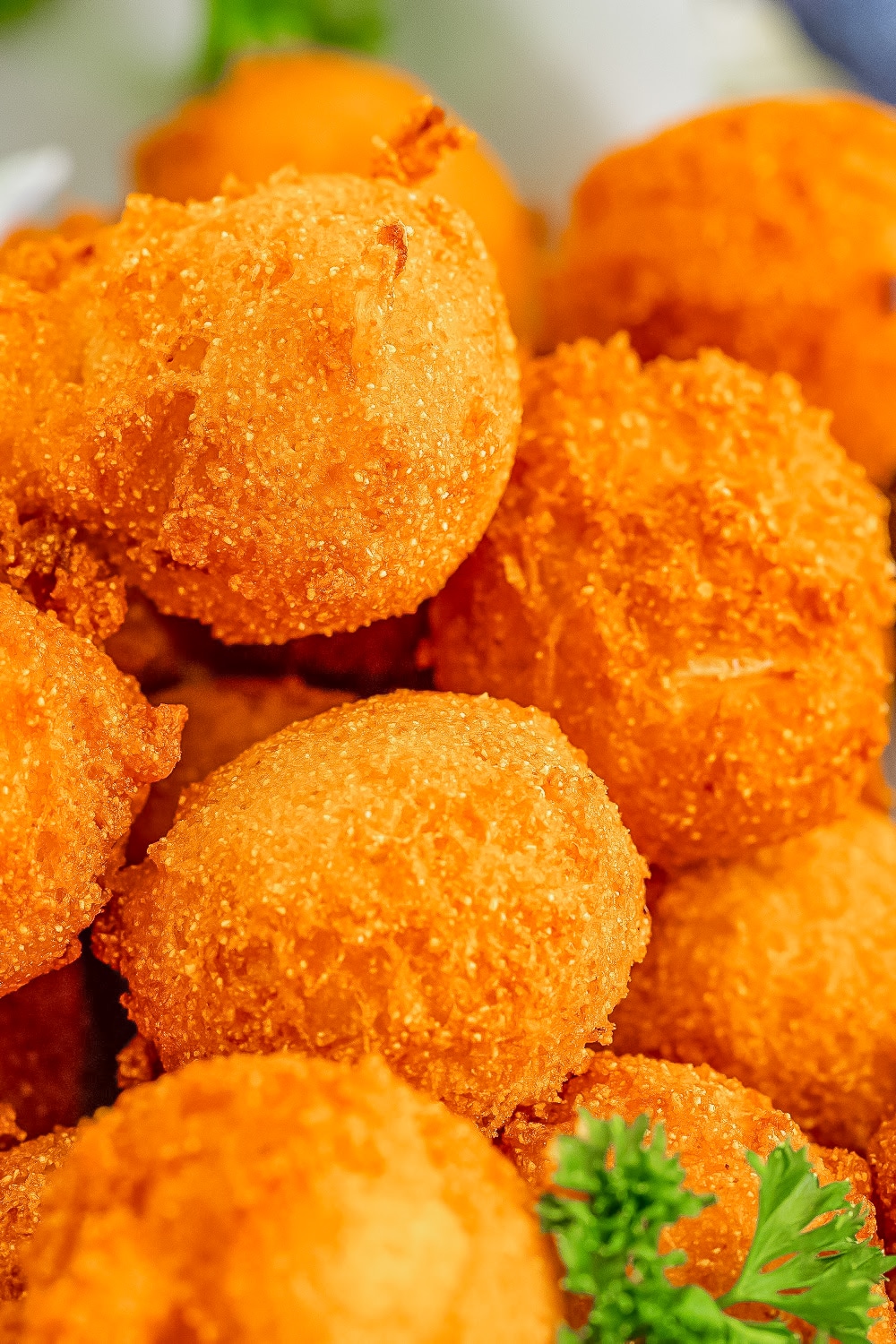 A close up of golden brown hush puppies in a pile with parsley garnish.