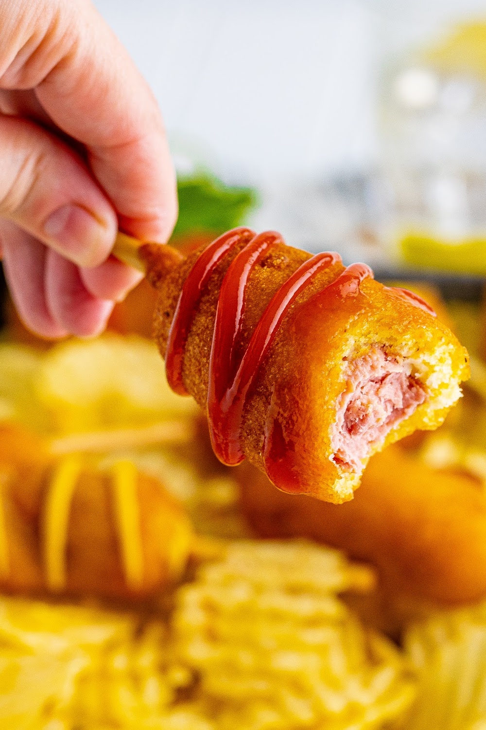 A woman's hand holding a corn dog with a bite missing.