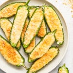 A white plate piled with jalapeno poppers with panko crumbs sprinkled around it.