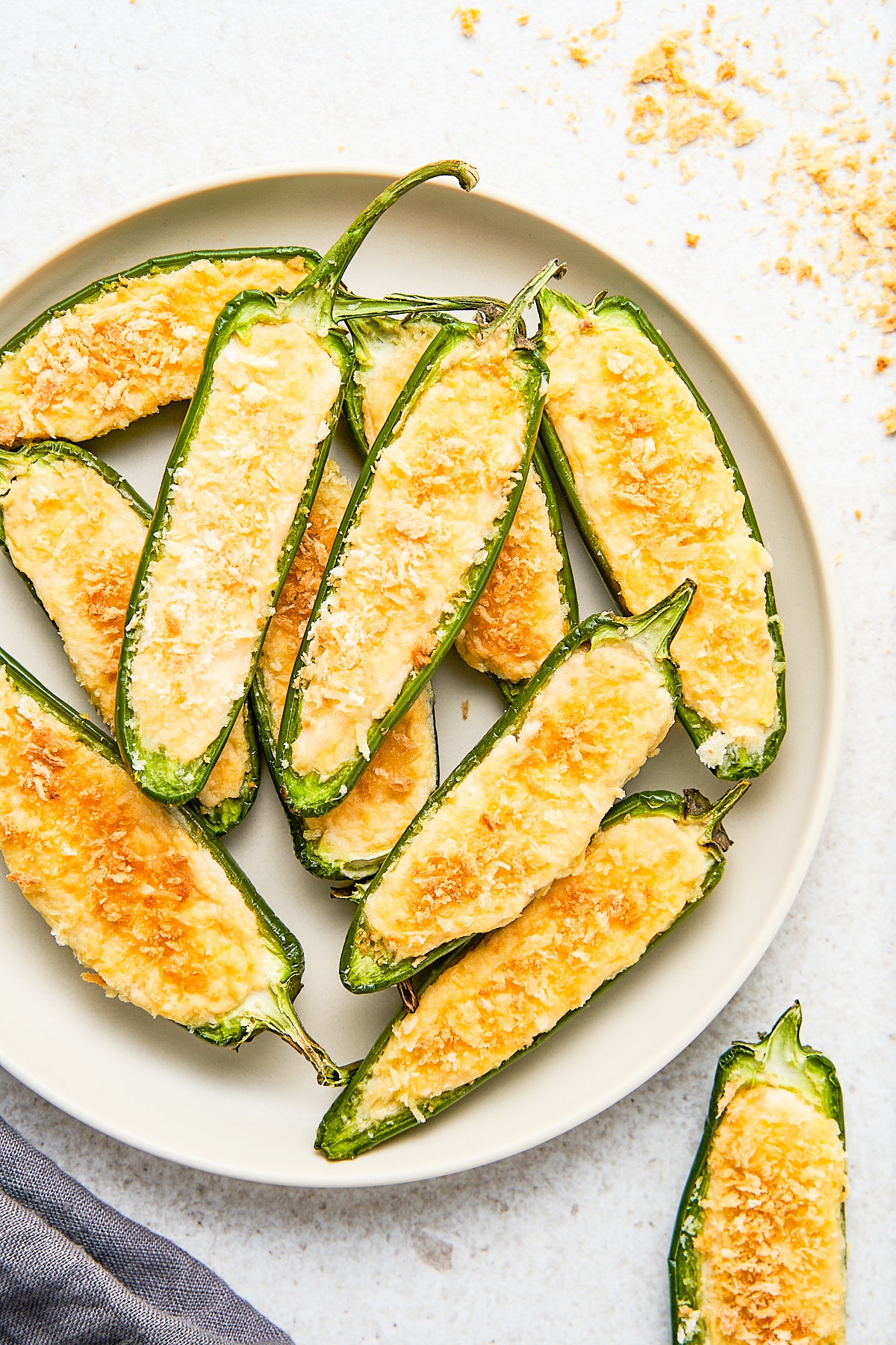 A white plate piled with jalapeno poppers with panko crumbs sprinkled around it.