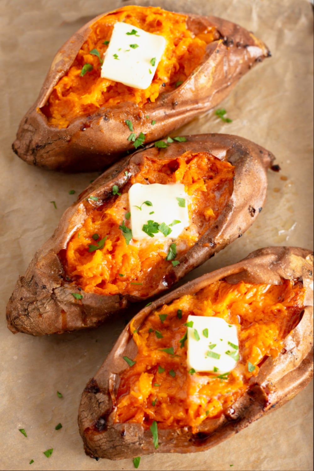 Three baked sweet potatoes with butter on parchment paper