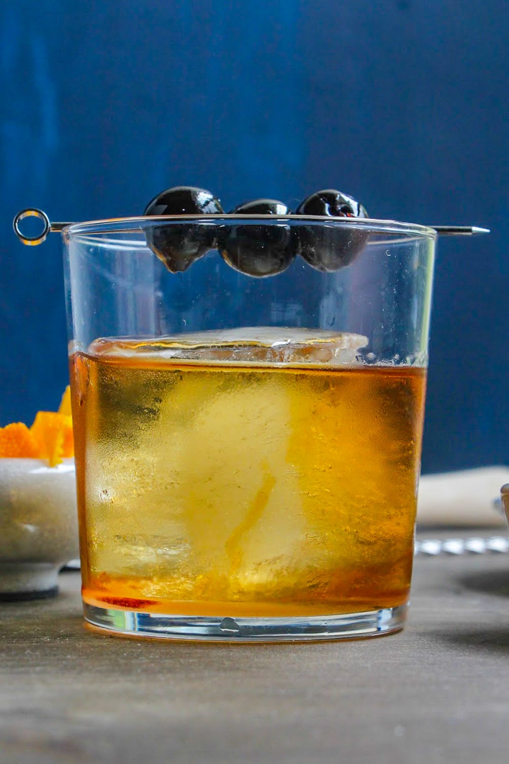 An Old Fashioned in a clear glass with a pick of cherries resting across the rim.