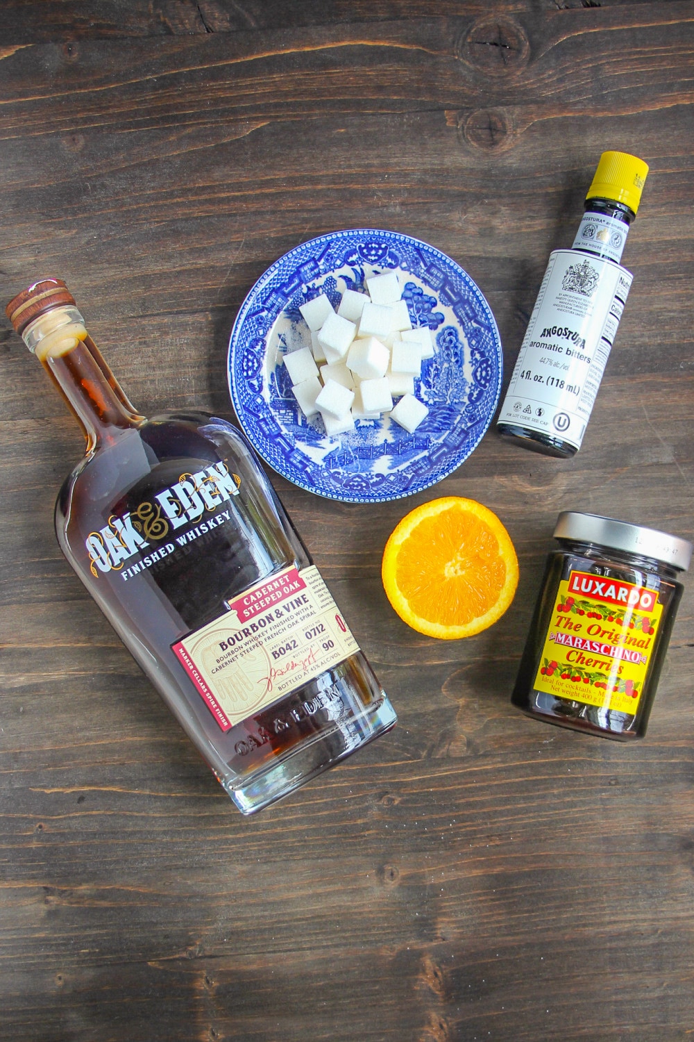 Ingredients needed to make a Old Fashioned presented on a wood table top.