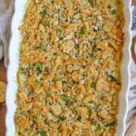 A white serving dish with chicken casserole garnished with parsley and poppy seeds.