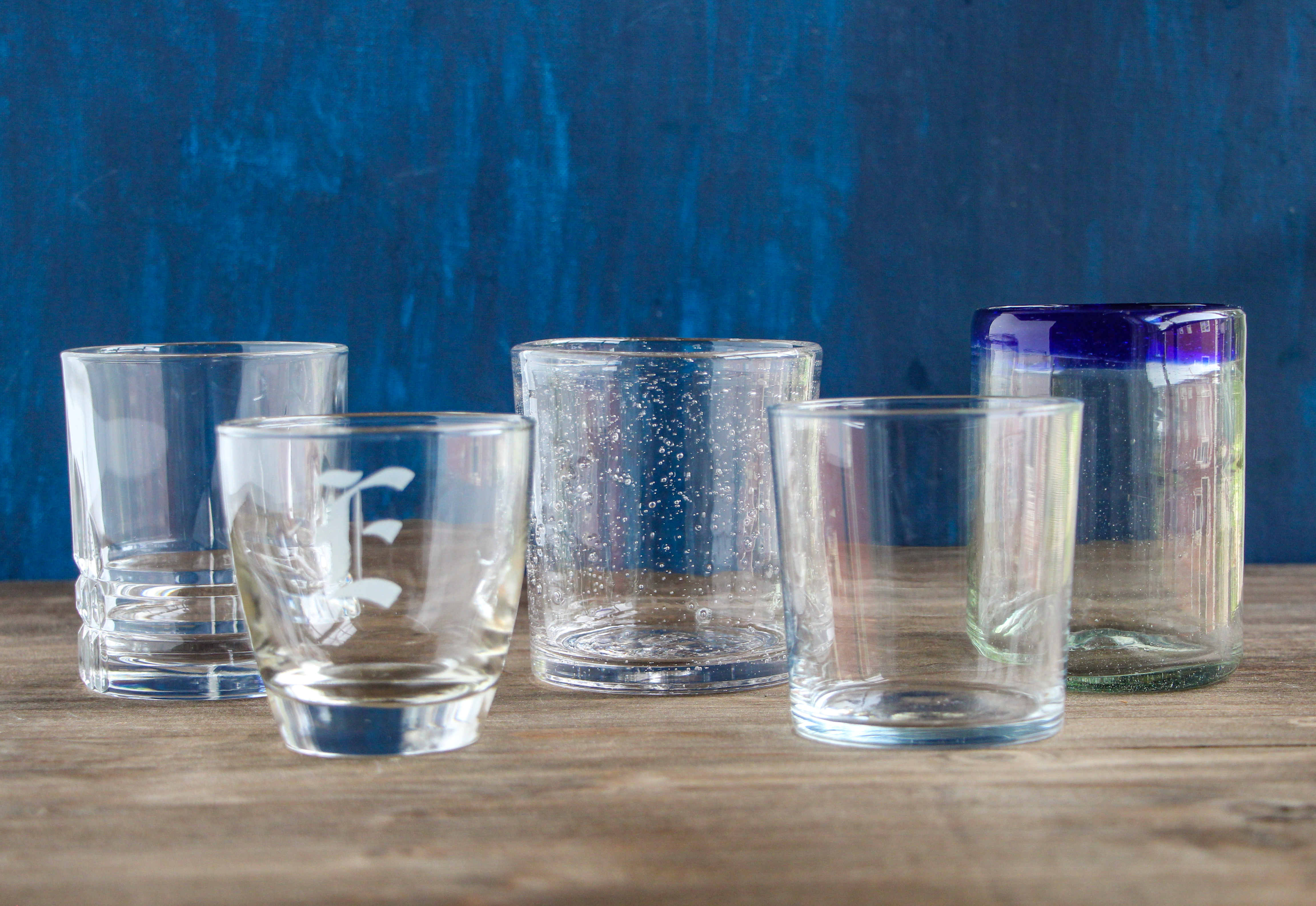 Five different styles of low ball cocktail glasses on a wood table top.
