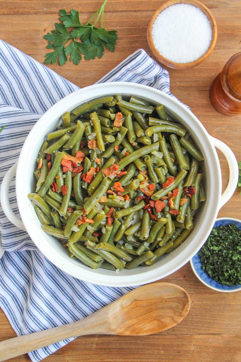 Green beans in a while serving bowl with handles on a blue and white stripe dish towel.
