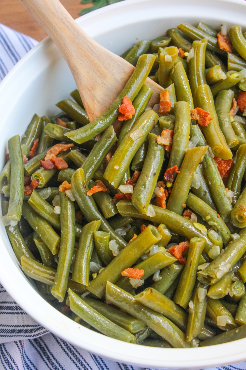Green Beans in a white serving bowl being scooped by a wooden spoon.