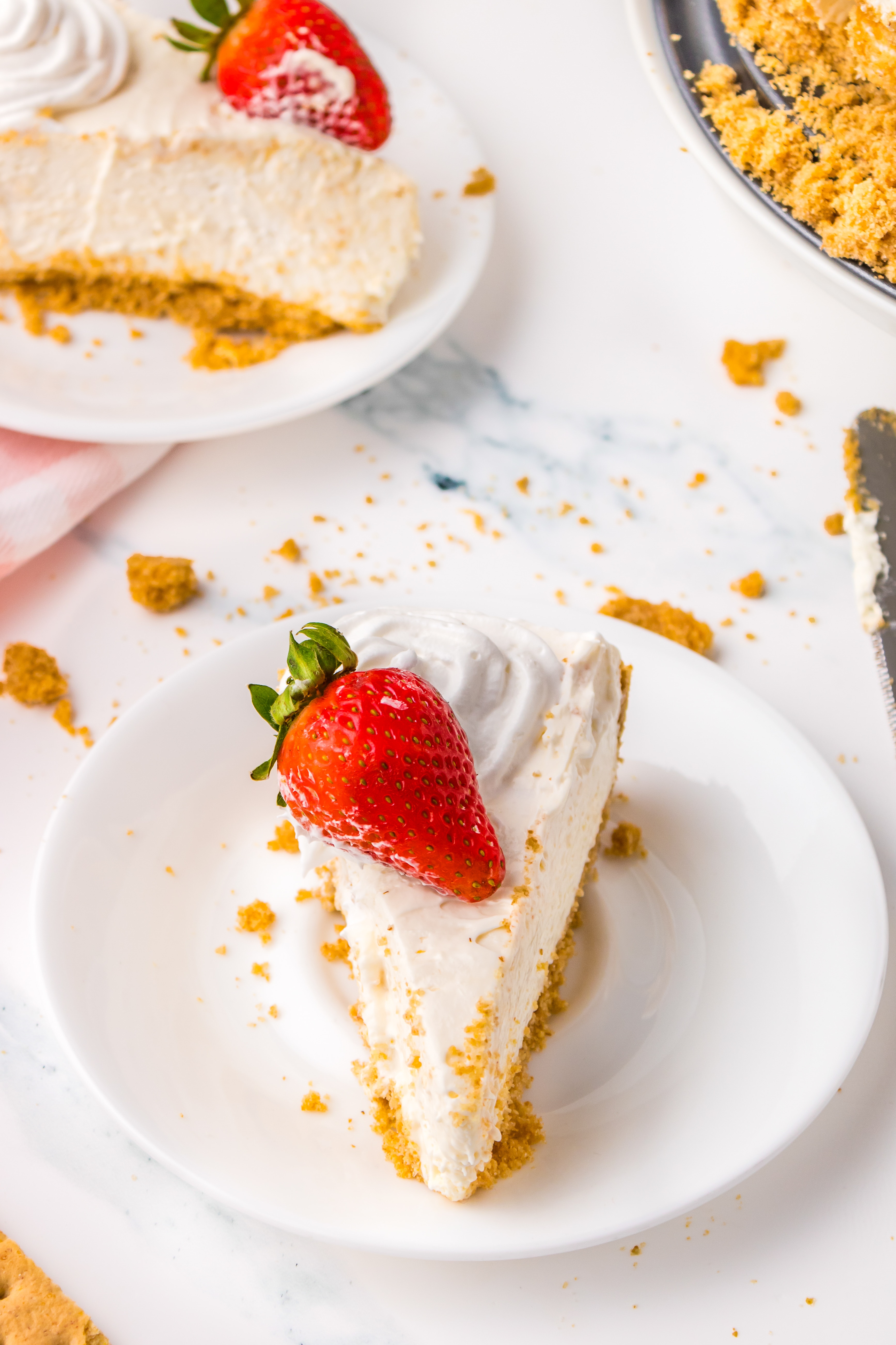 A slice of No Bake Cheesecake topped with a fresh strawberry on a white dessert plate.