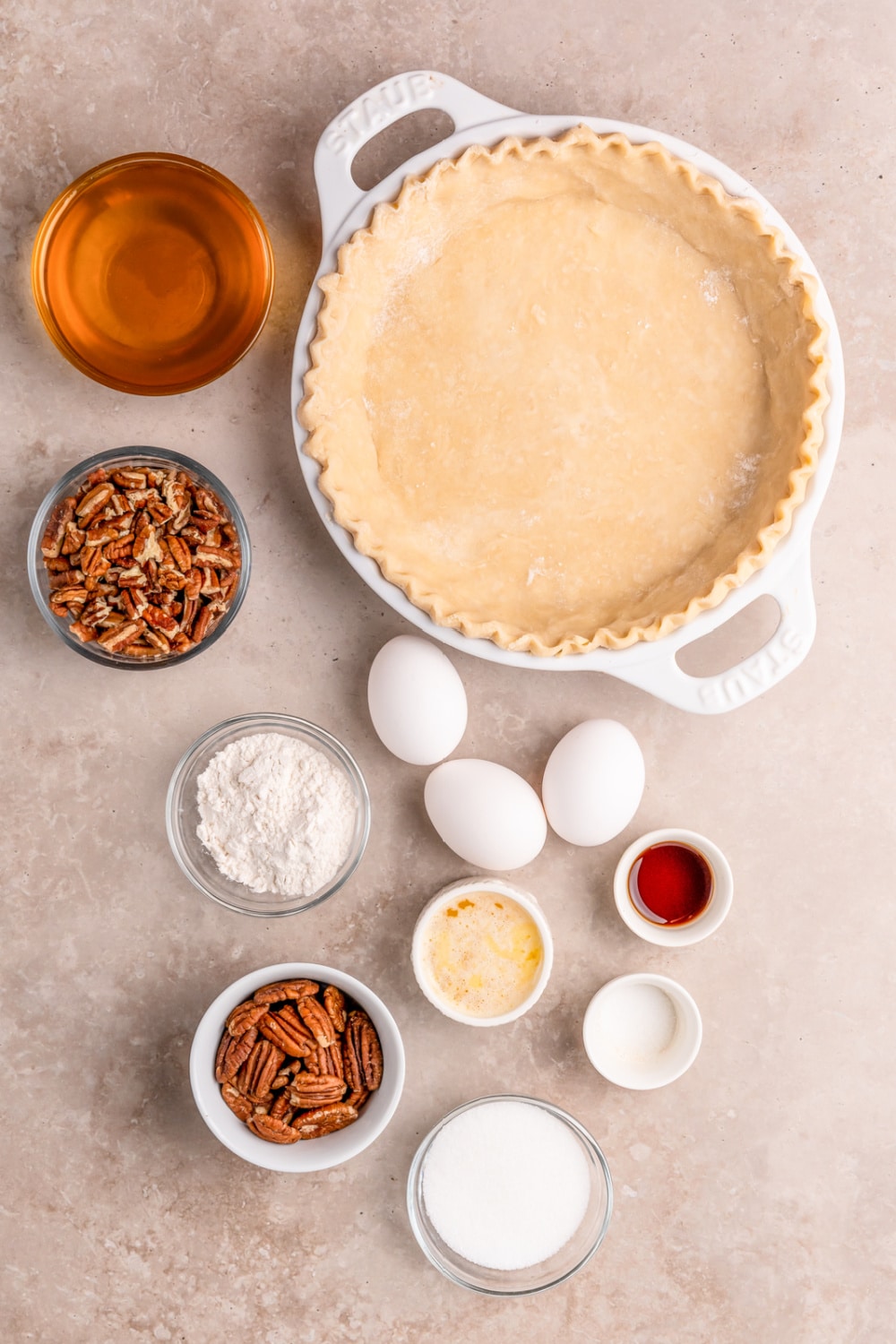 Measured ingredients needed to make this Honey Pecan Pie presented in glass bowls on a grey background.