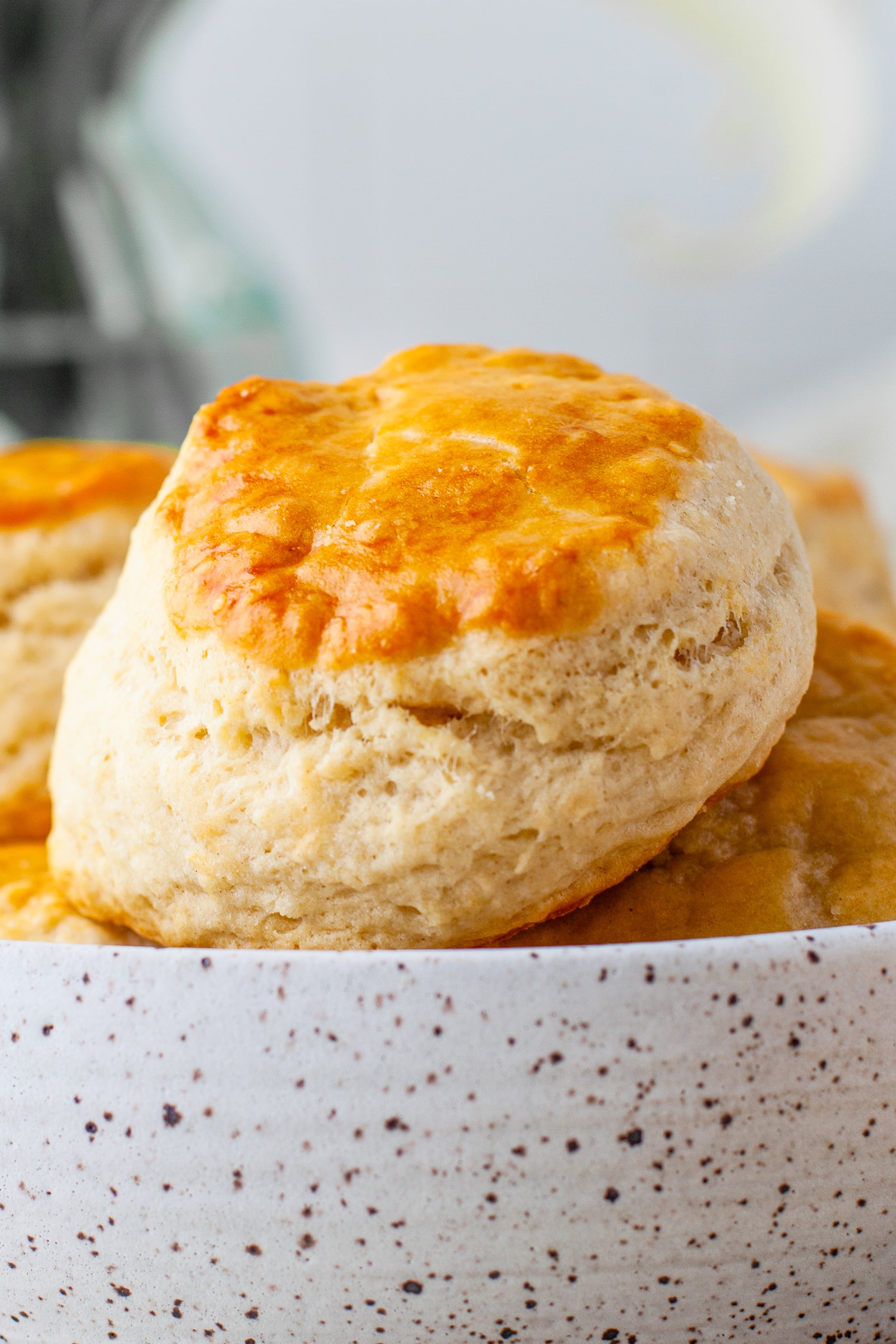 A biscuit with golden brown top sits on top of a bowl of biscuits.