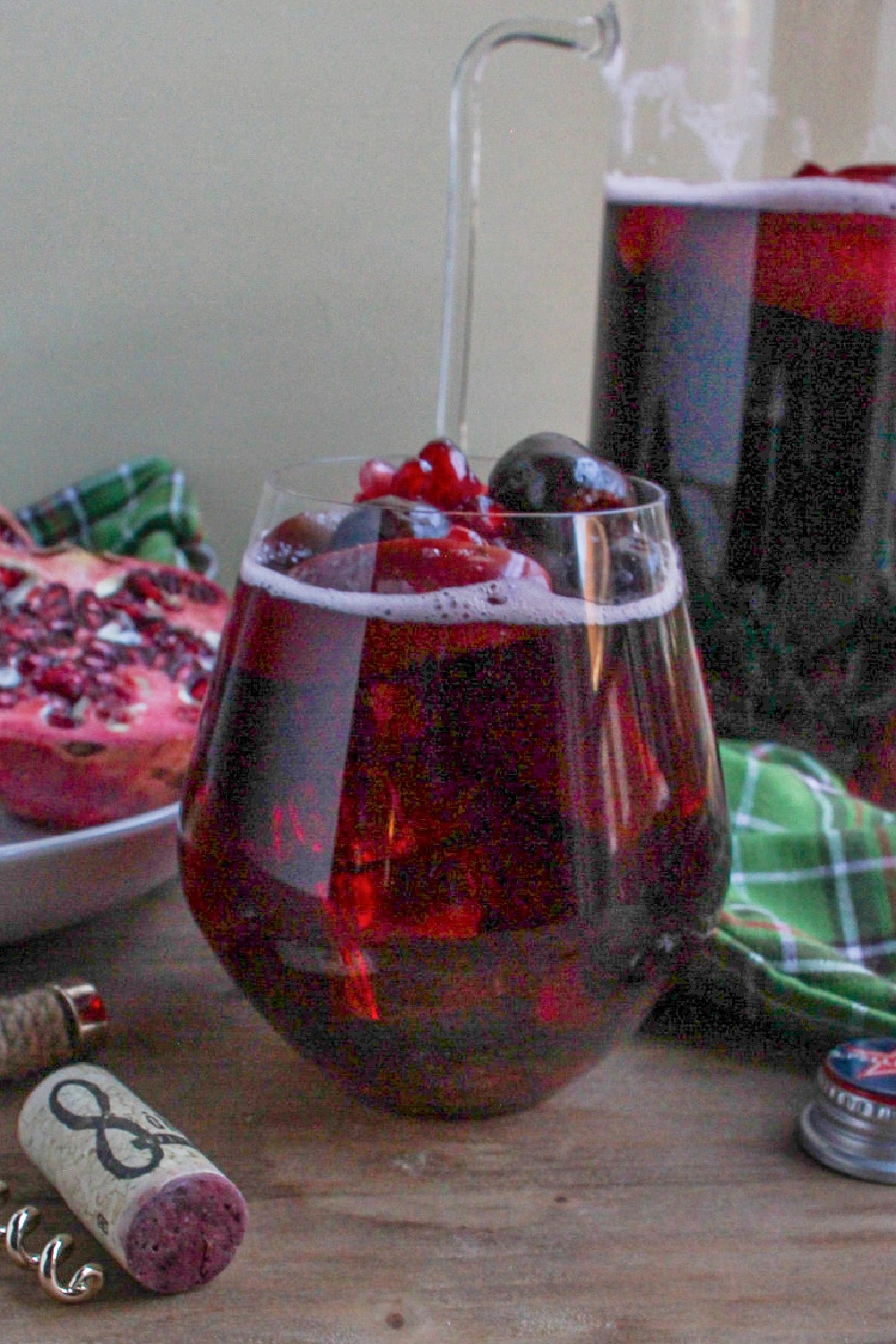 A glass of sangria sits in front of a pitcher of sangria and a sliced pomegranate.