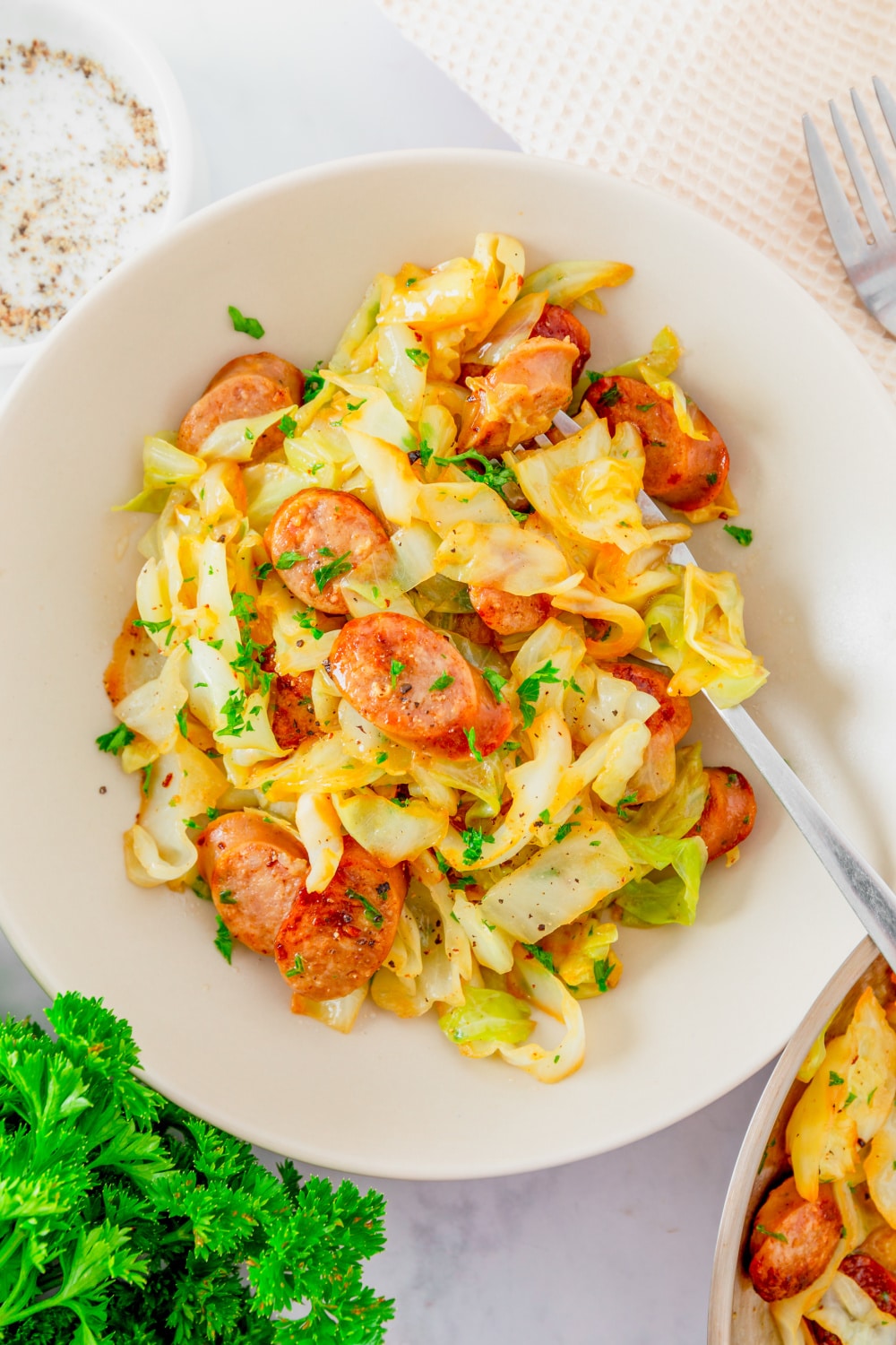 Cabbage and Sausage in a white bowl with fork.