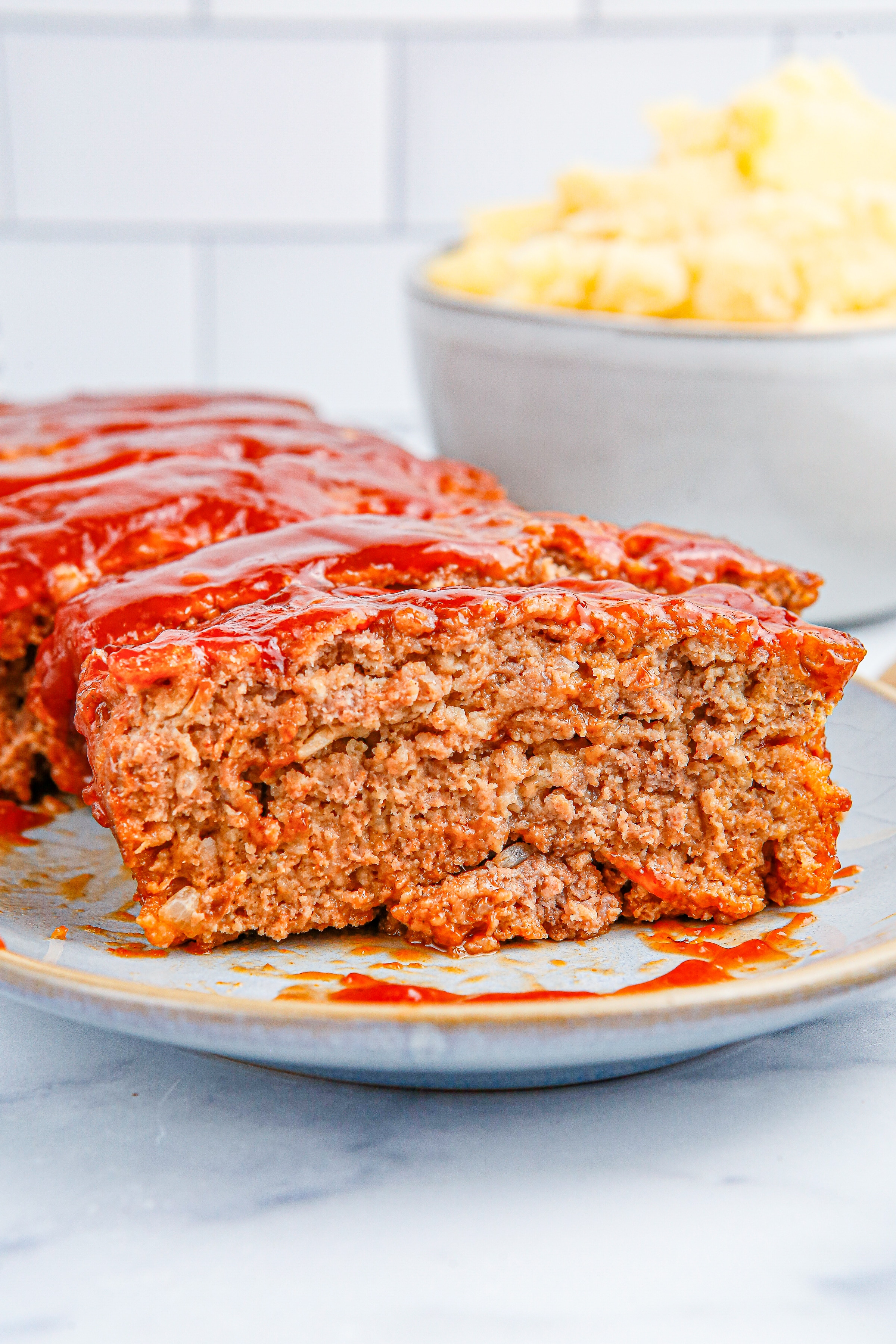 Slices of meatloaf with tomato sauce glaze on a white serving platter.