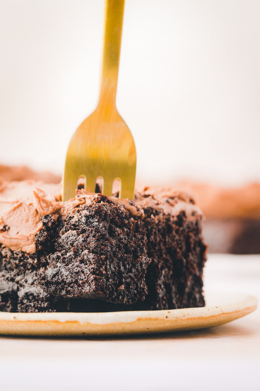 A gold fork cuts the corner of a slice of chocolate sheet cake.