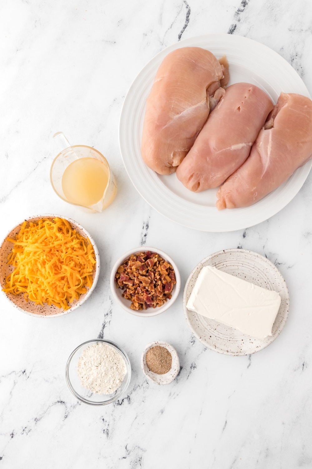 Measured ingredients needed to make the chicken, bacon, ranch, cheese mixture presented on a white marble countertop.