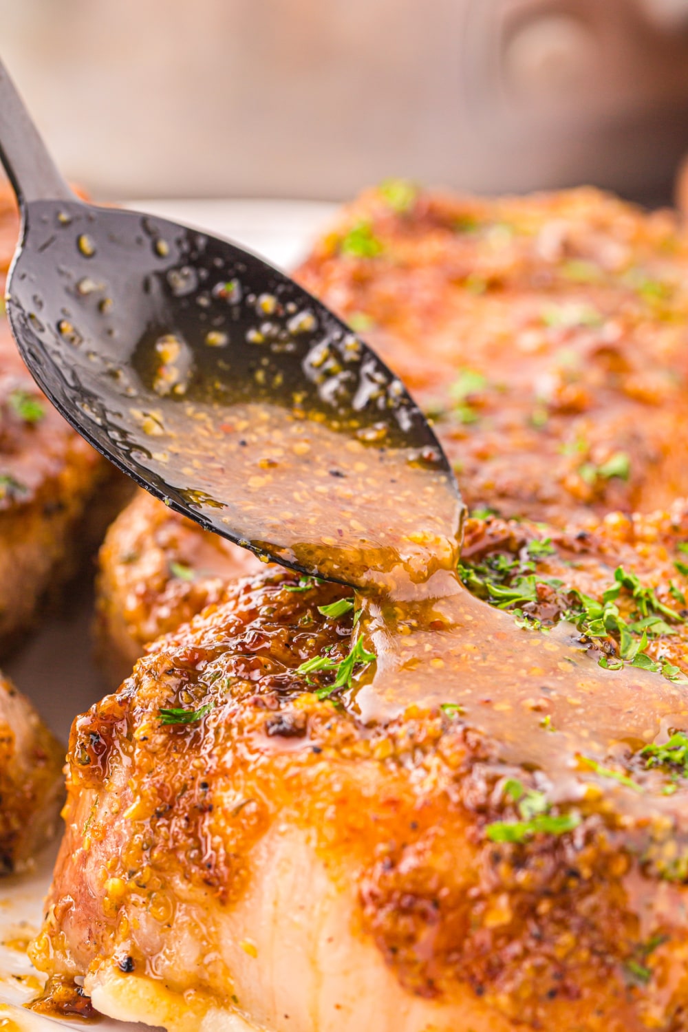 A spoon pouring honey mustard glaze over a pork chop.