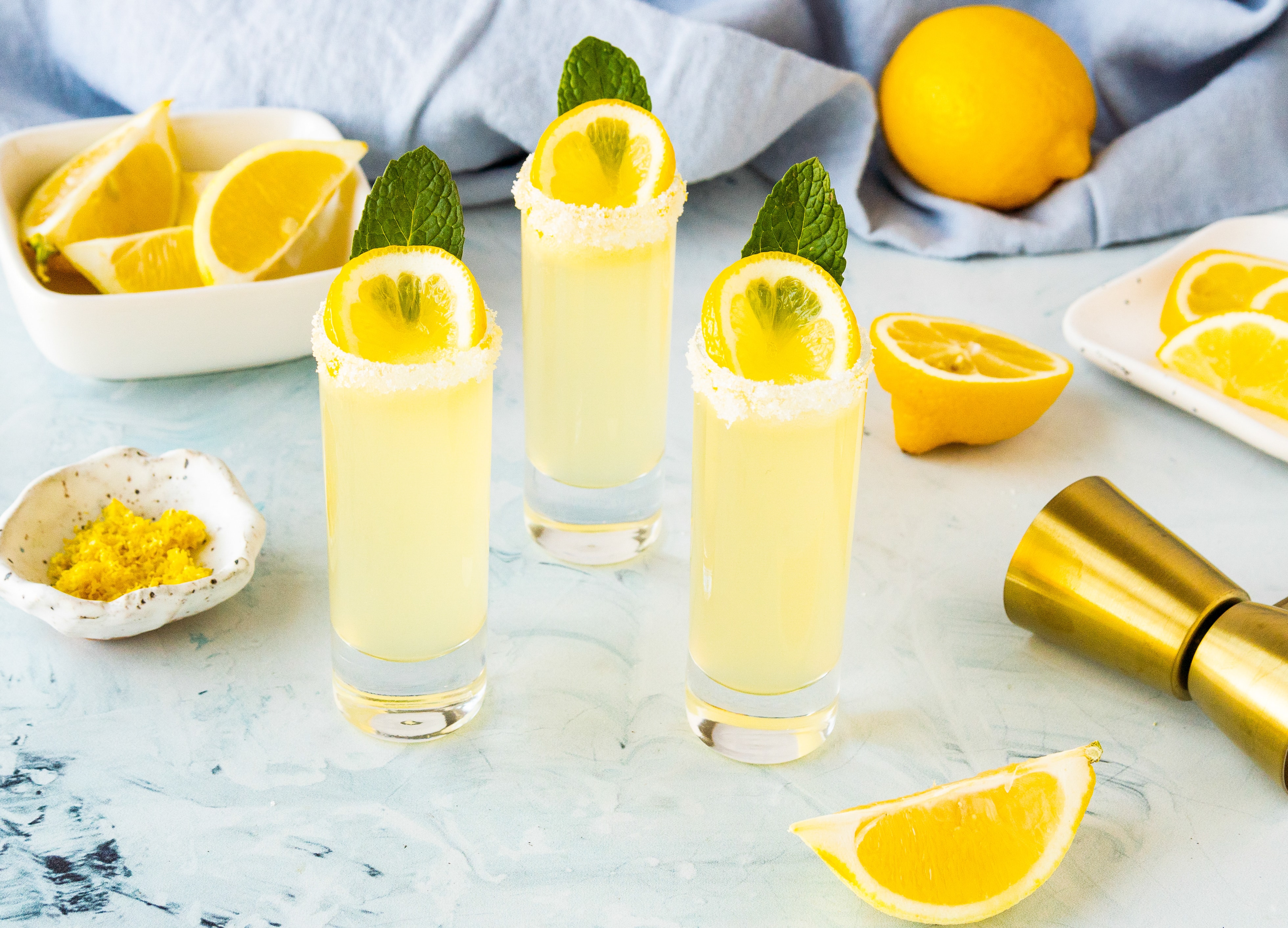 Three Lemon Drop Shots in tall shot glasses with a lemon slices.