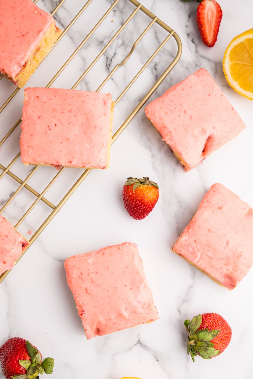 Strawberry Blondies with frosting on a cooling rack resting on a white marble countertop.