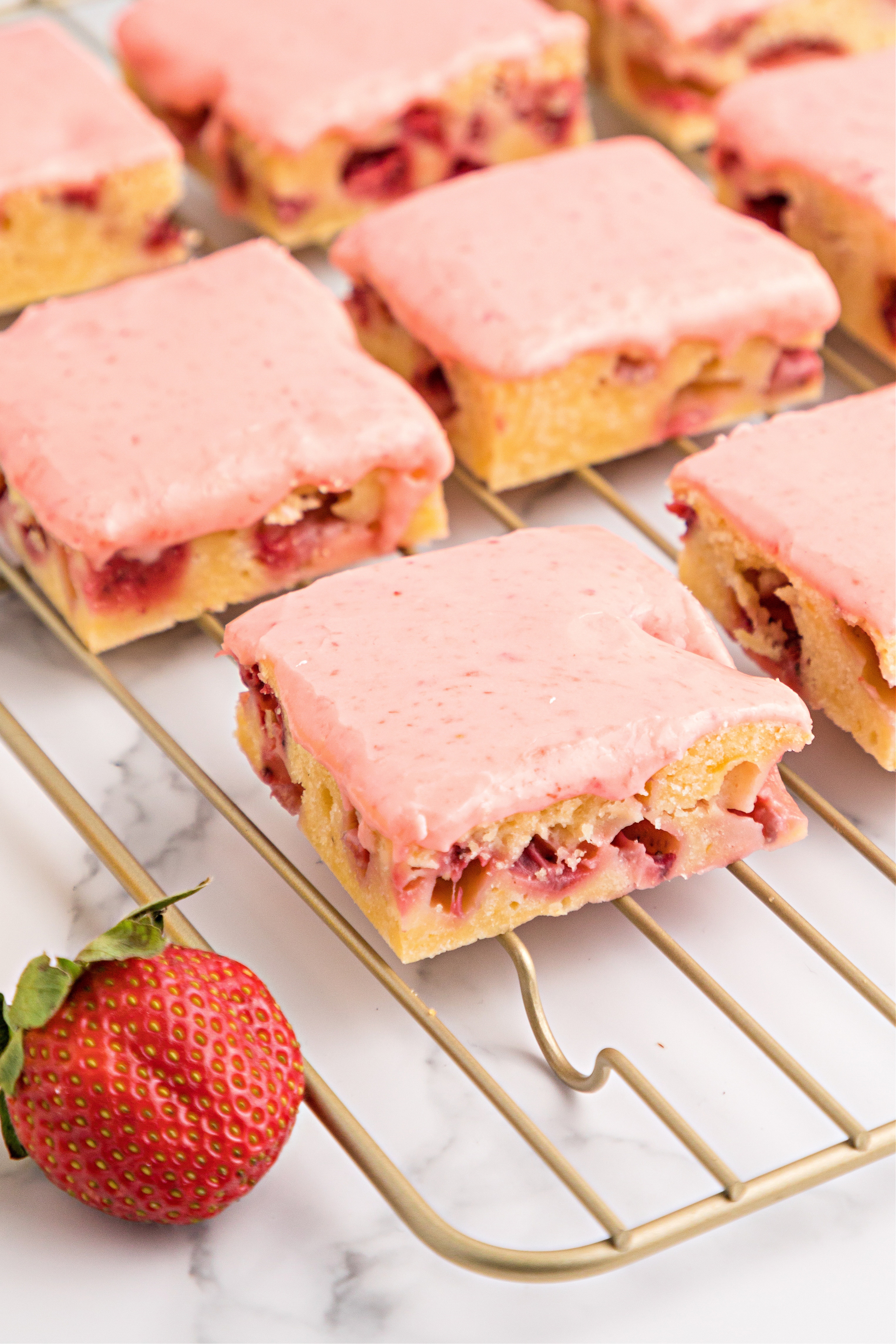 Blondies with strawberry glaze on a cooling rack.