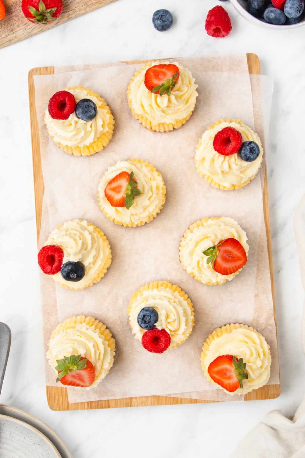 Mini Cheesecakes topped with strawberries, blue berries, and raspberries on white parchment paper.