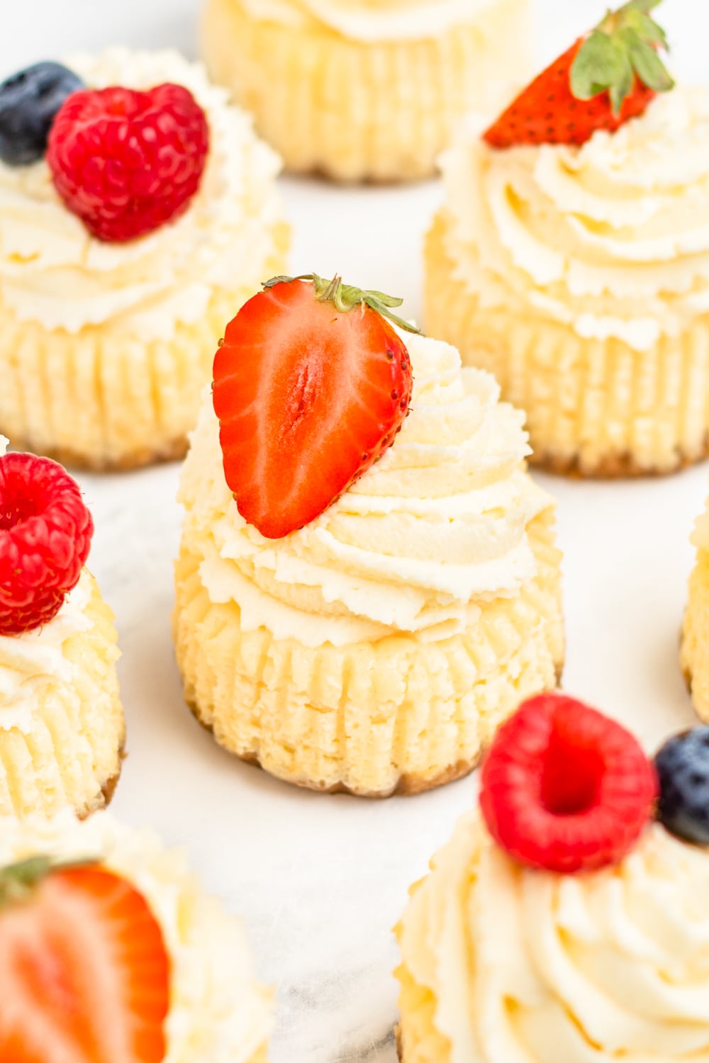Mini Cheesecakes topped with whipped cream and fresh berries on white parchment paper.