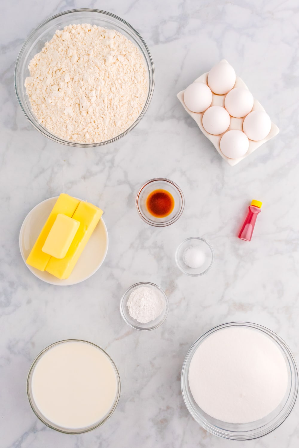 Measured ingredients needed to make a yellow sheet cake presented on a white marble countertop.