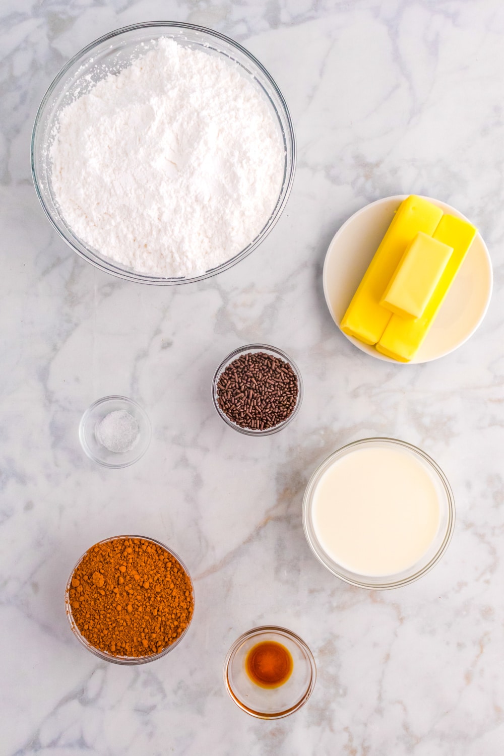 Measured ingredients needed to make chocolate frosting presented on a white marble countertop.