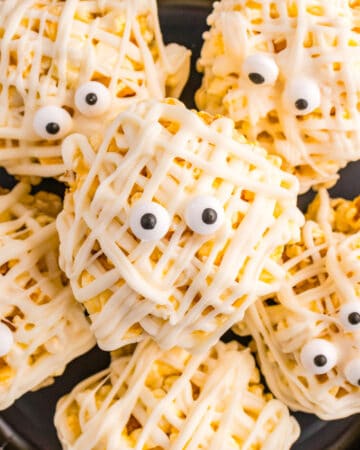 Halloween Popcorn Balls that look like wrapped mummies in a black plate.