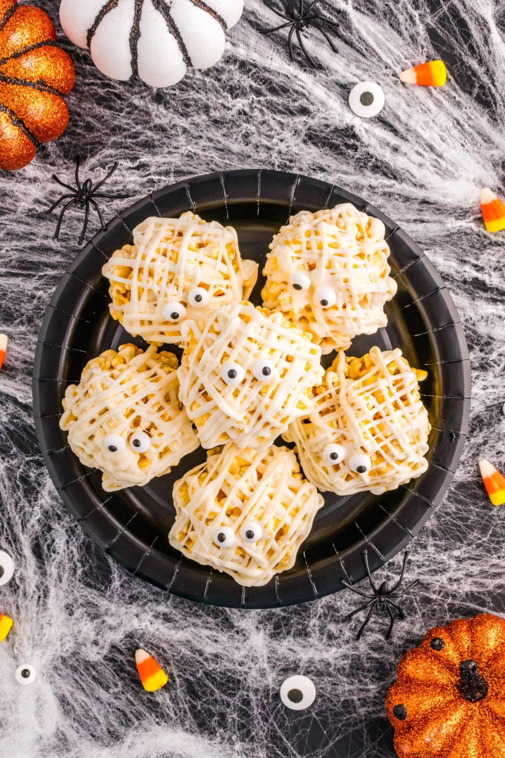 Mummy Popcorn Balls on a black plate sitting on a backdrop of spider webs.