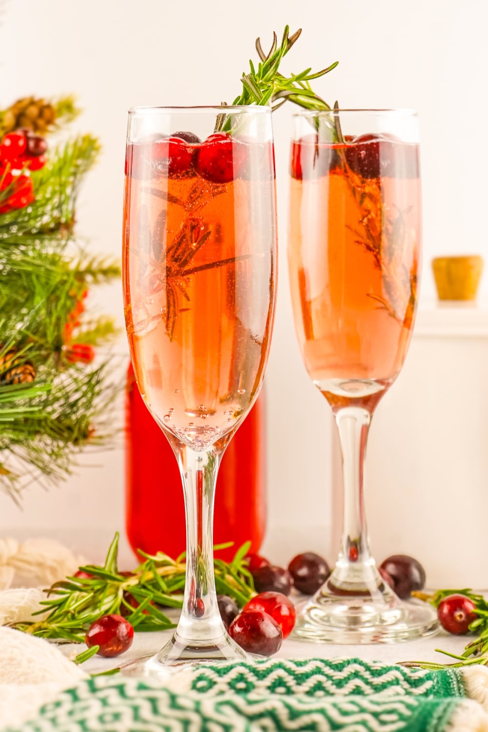 Two champagne flutes filled with Cranberry Mimosa garnished with rosmary.