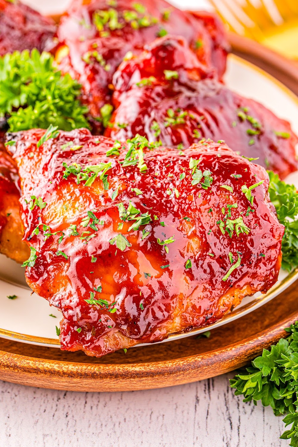 Baked BBQ Chicken Thigh garnished with parsley on a white dinner plate.