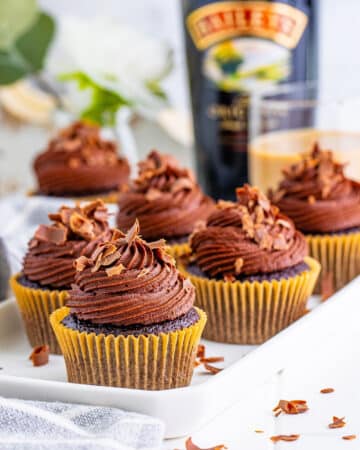 Six cupcakes on a white tray sit in front of a of a bottle of Bailey's Irish Cream.