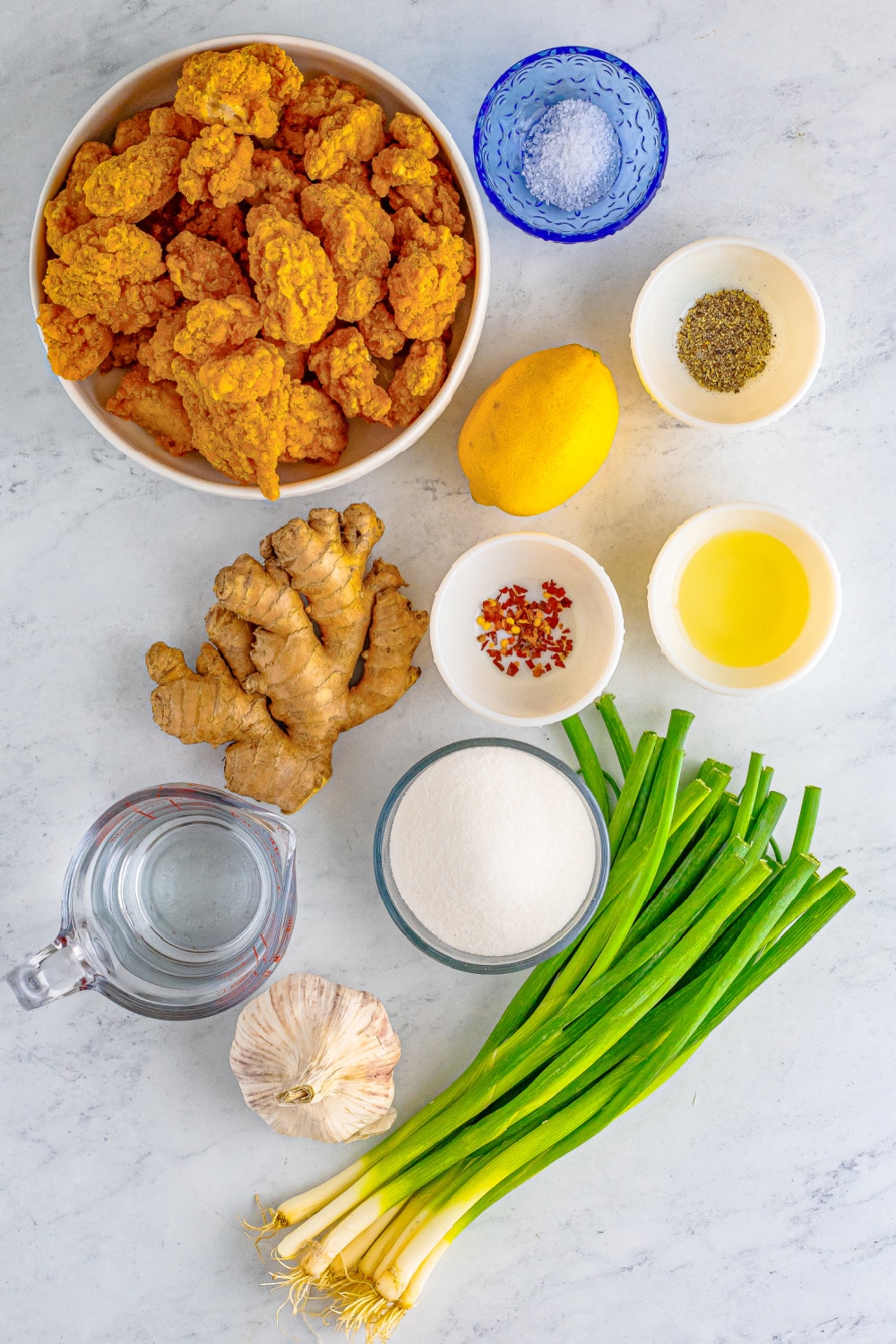 Measured ingredients needed to make lemon chicken presented on a white marble countertop. 