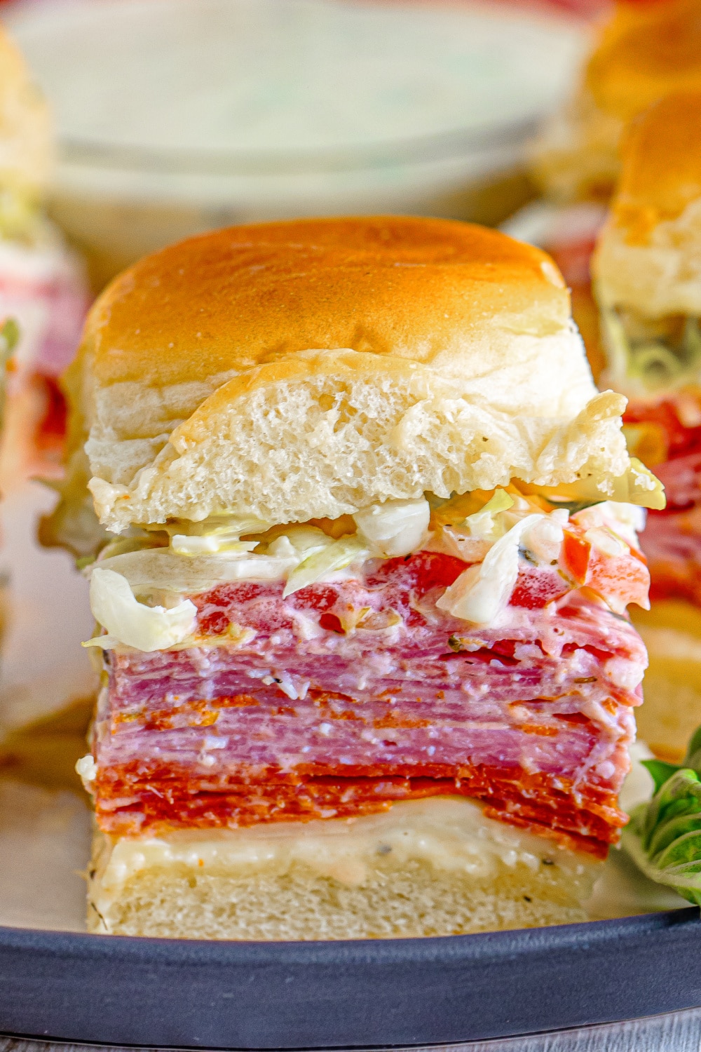 A single slider stacked high with deli meats and cheeses and sandwich sauce.