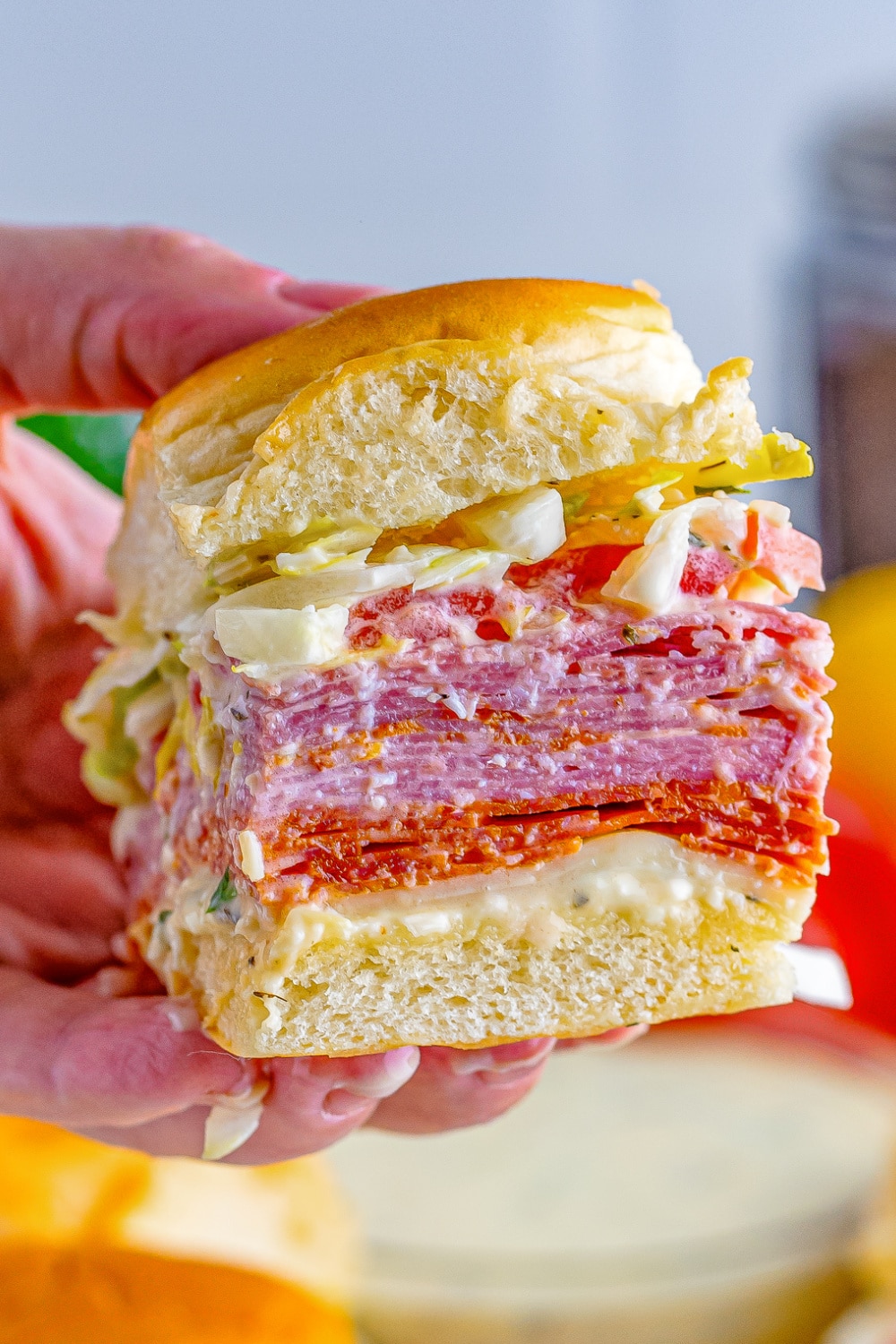 A woman's hand holds a slider piled high with meat, cheese, veggies and sauce.