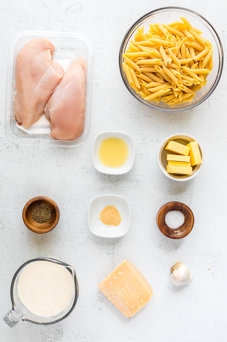 Ingredients needed for making Garlic Parmesan Pasta with Chicken presented on a white marble countertop.