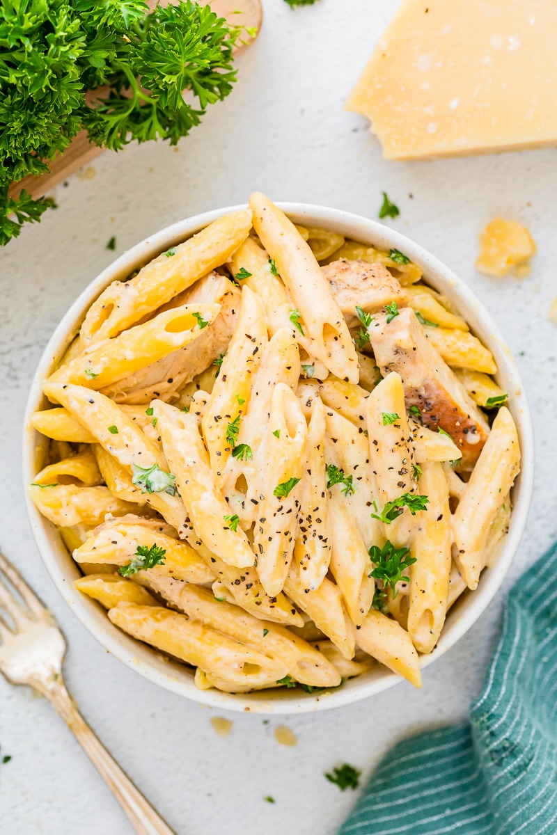 Pasta in a white bowl with sliced chicken and parsley.