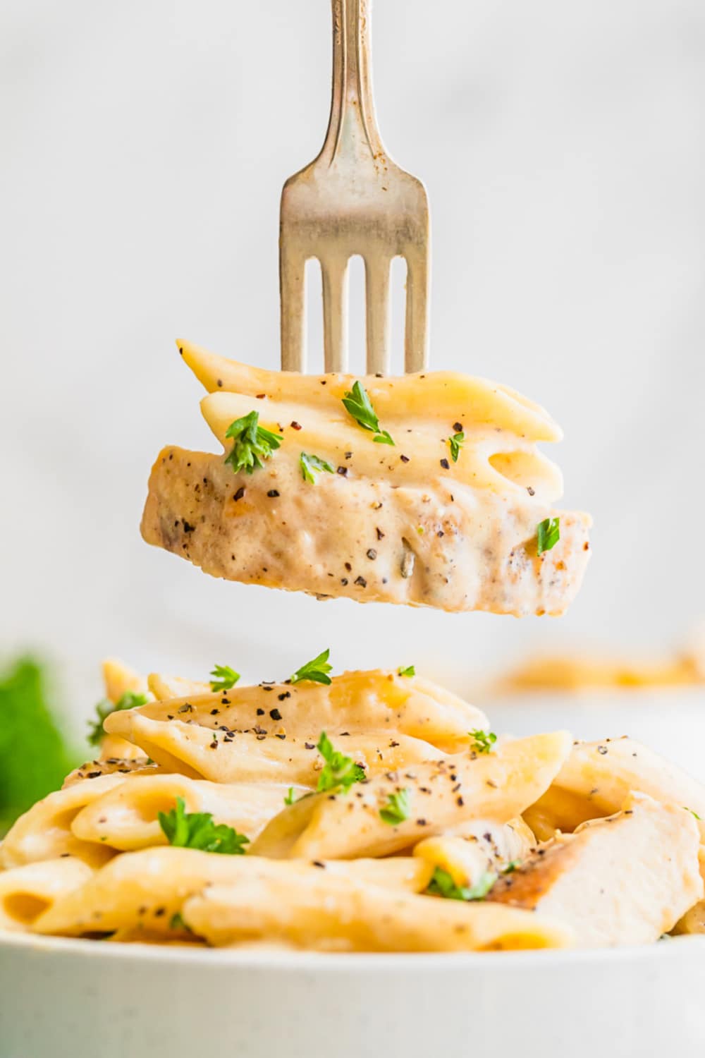 A fork with a bite of pasta and a sliced chicken on a fork.