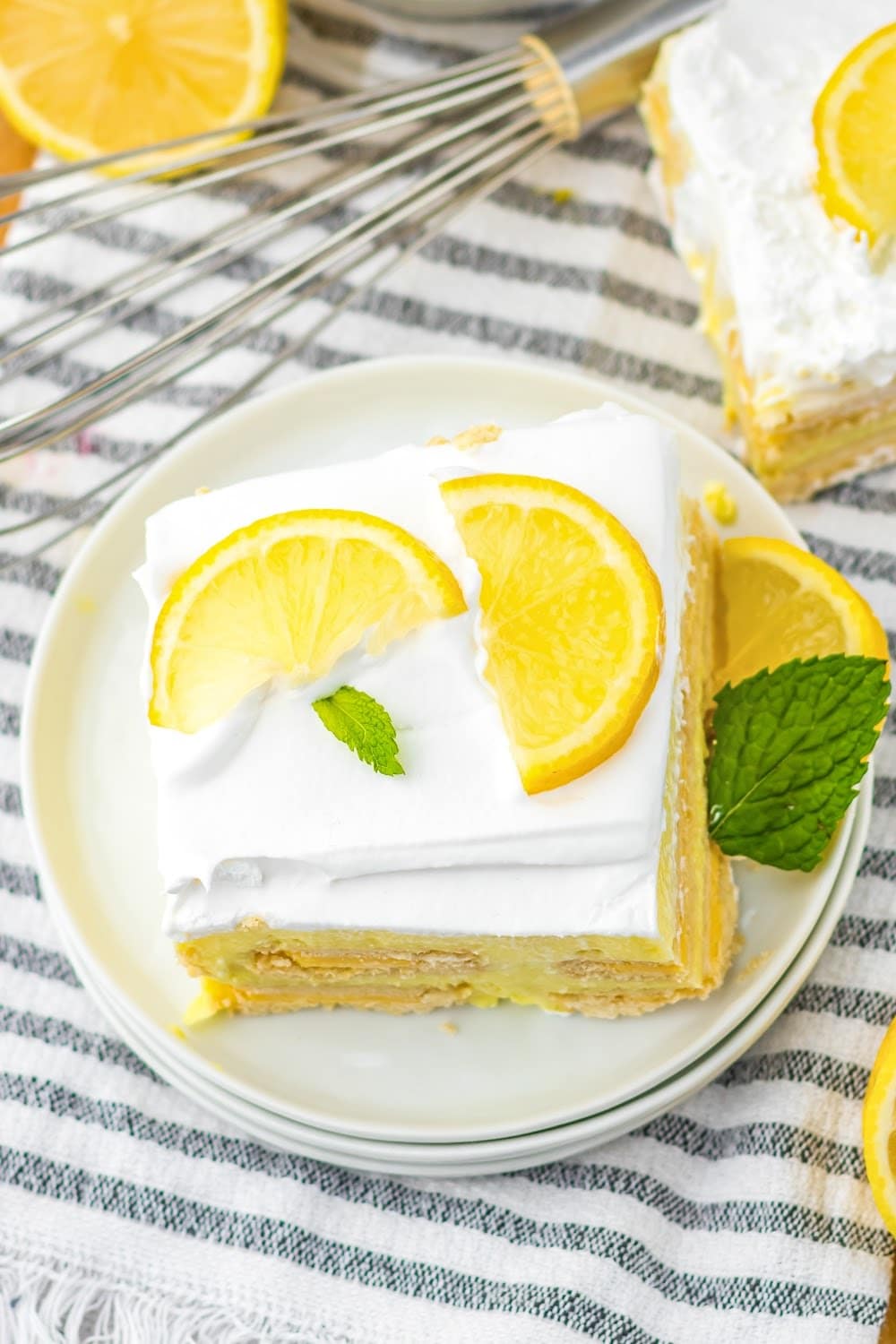 A slice of icebox cake topped with lemon slices and mint on a white plate.