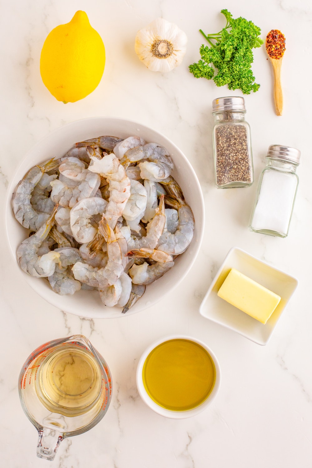 Ingredients needed to make Shrimp Scampi presented on a white marble countertop.
