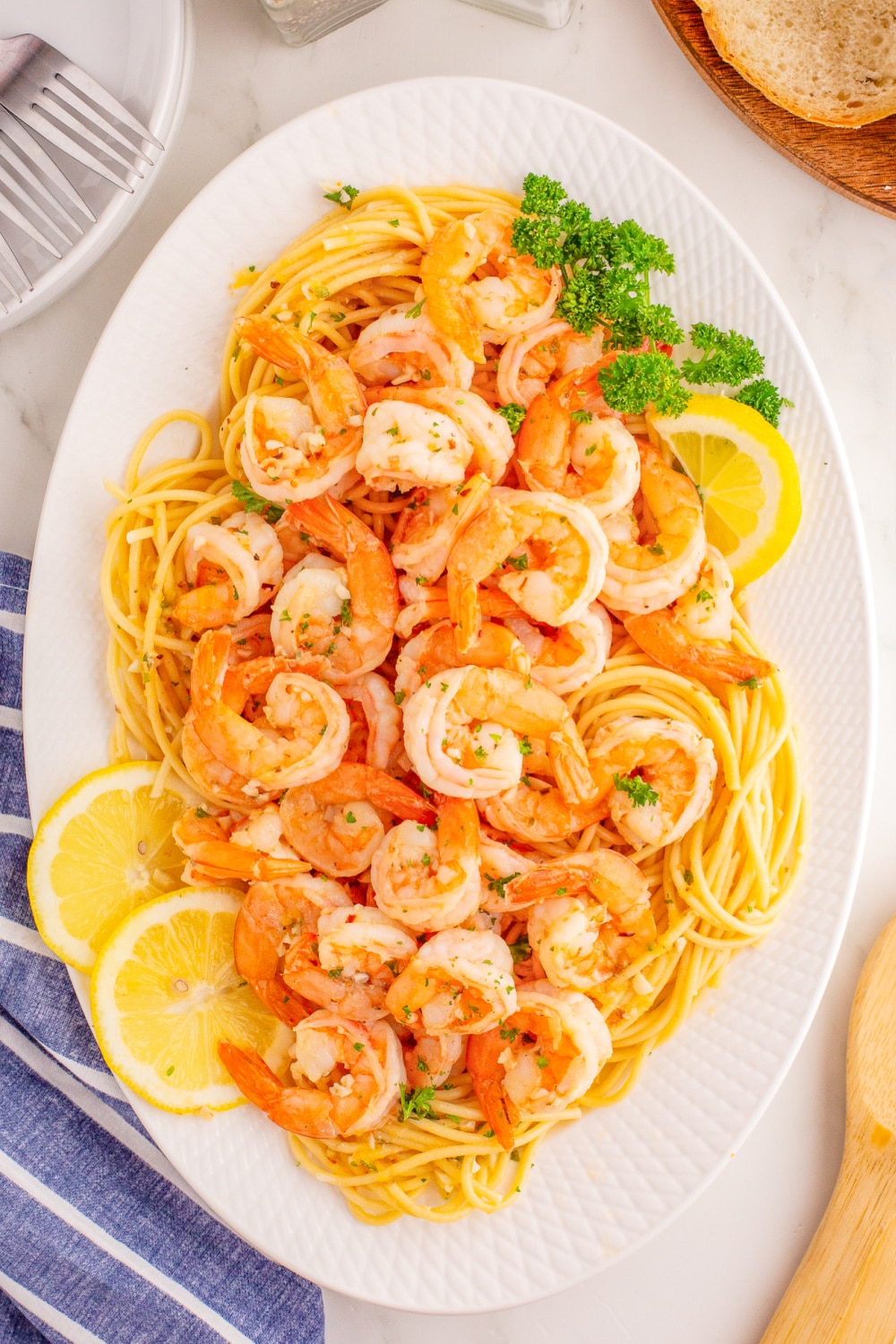 A white platter filled with pasta with shrimp scampi piled on top with lemon wedges.