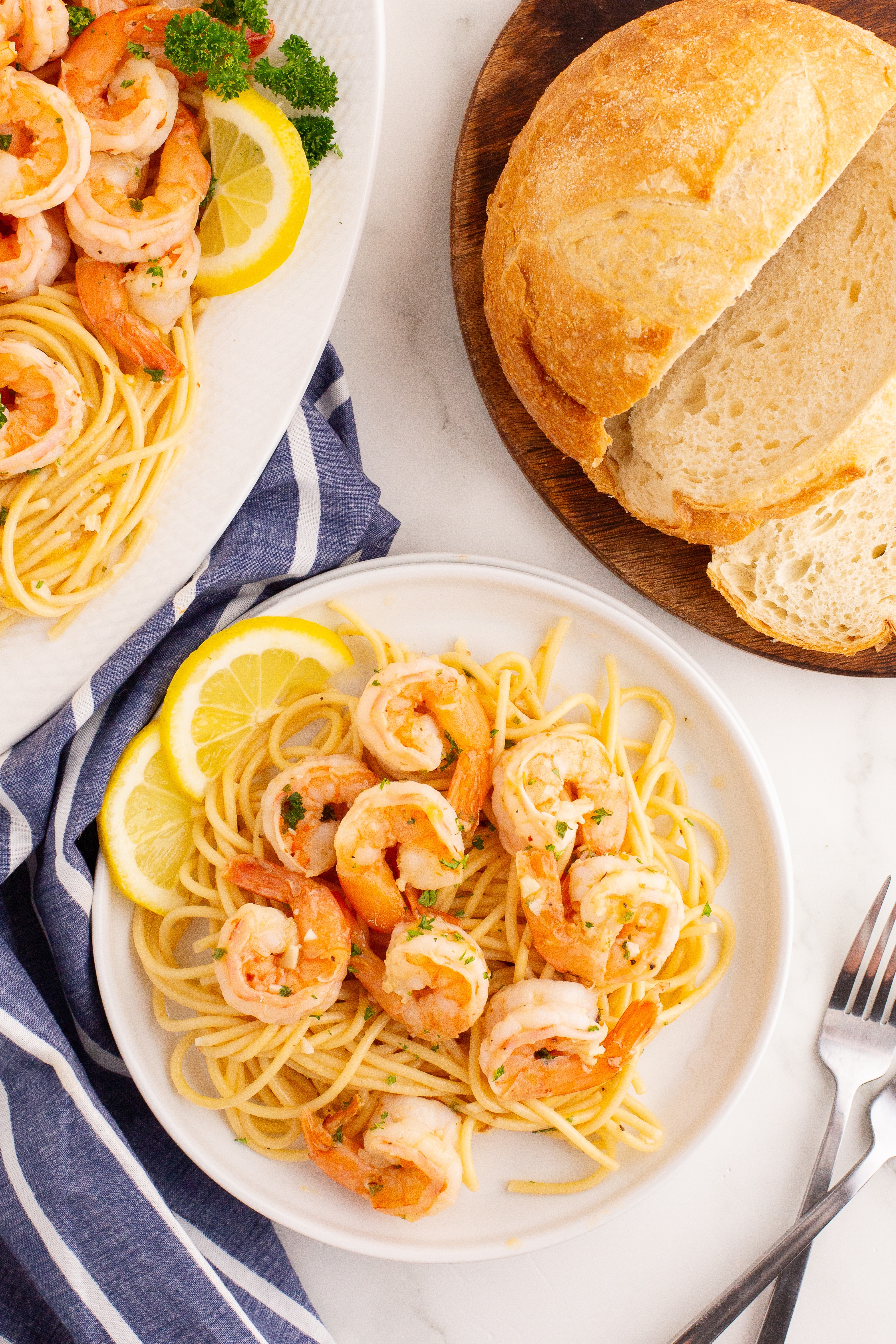 Shrimp pasta on plates next to a loaf of crusty bread.