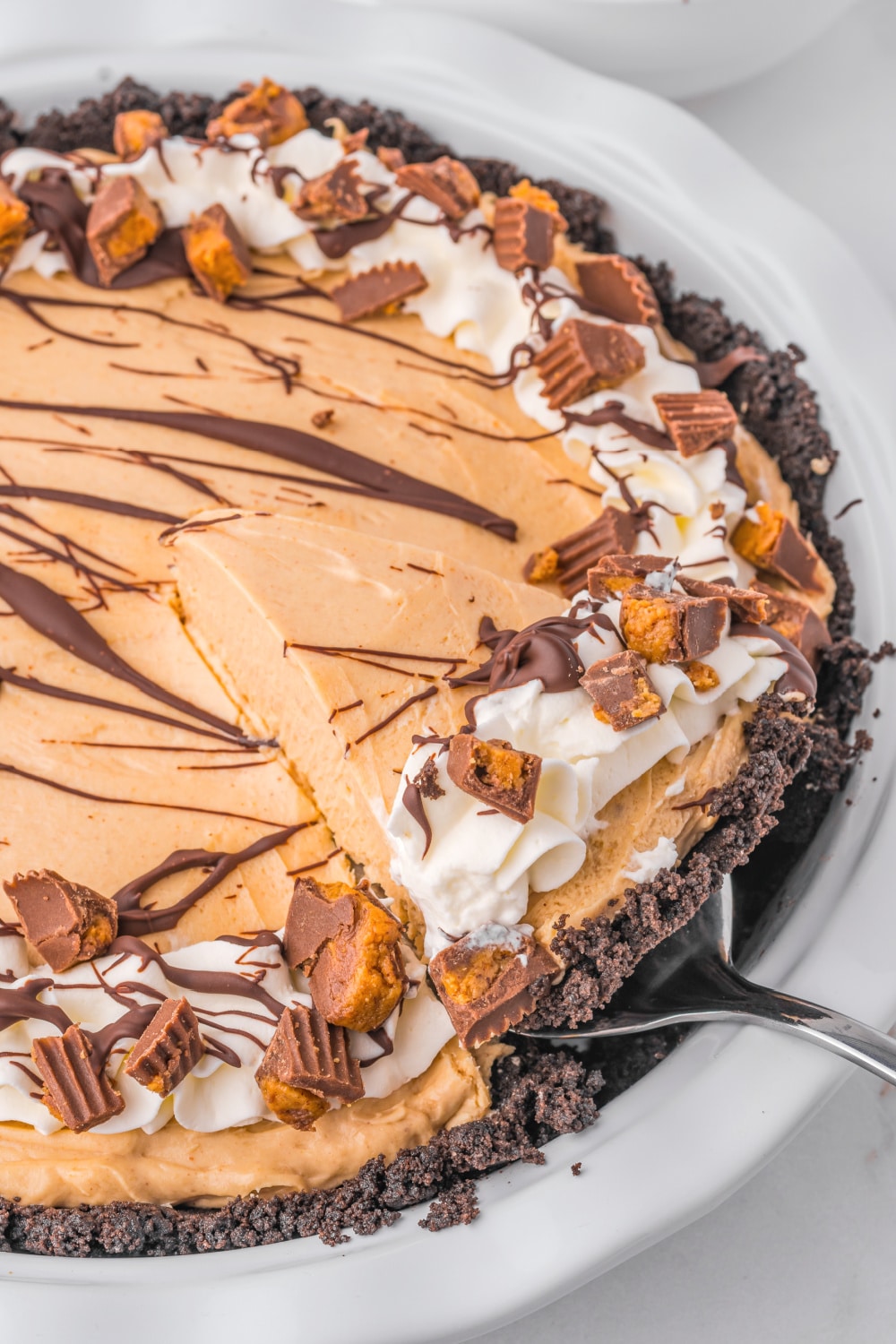 No Bake Peanut Butter Pie drizzled with chocolate syrup in a white pie plate.