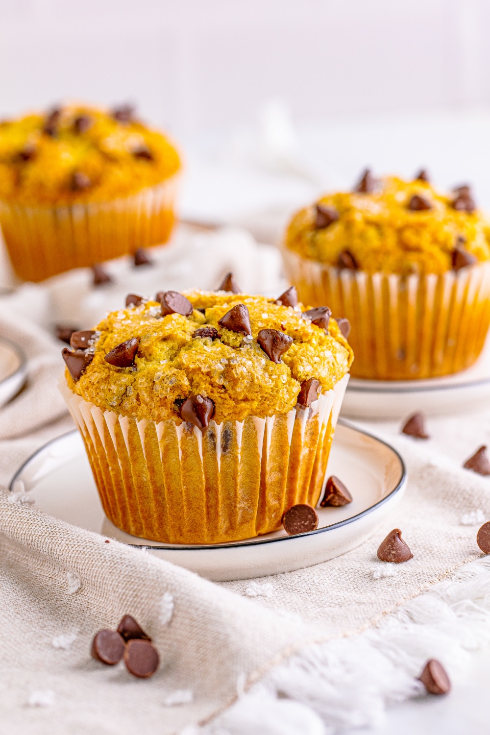 Three bakery style chocolate chip muffins in white muffin wrappers.