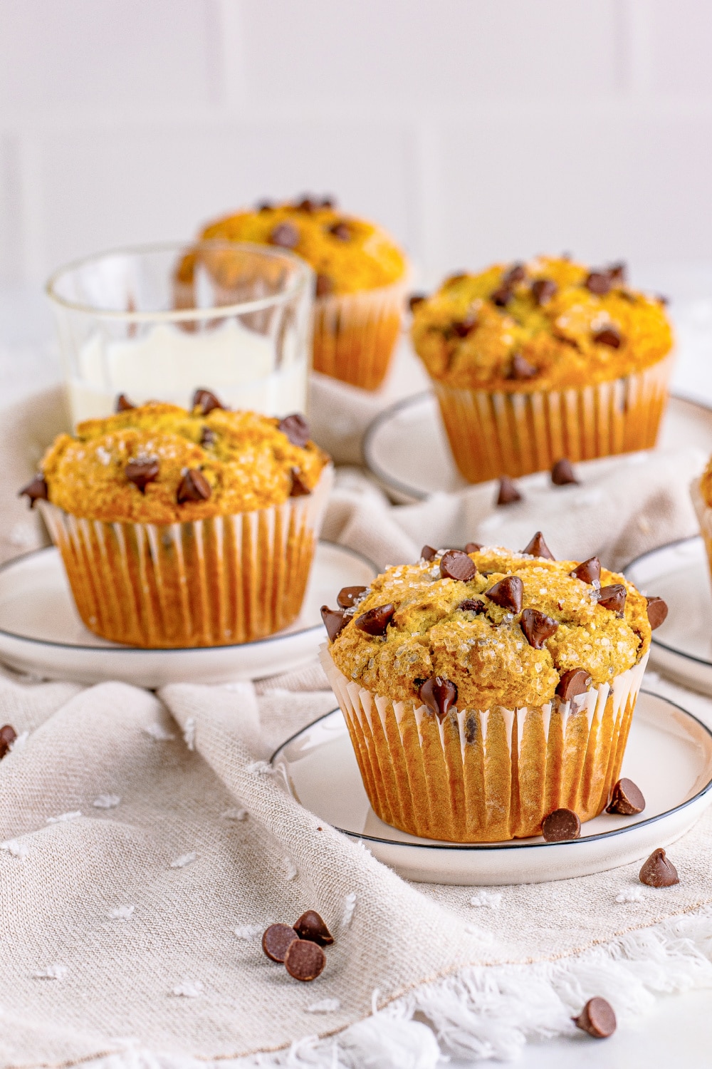 Four muffins full of chocolate chips on a table with a glass of milk.